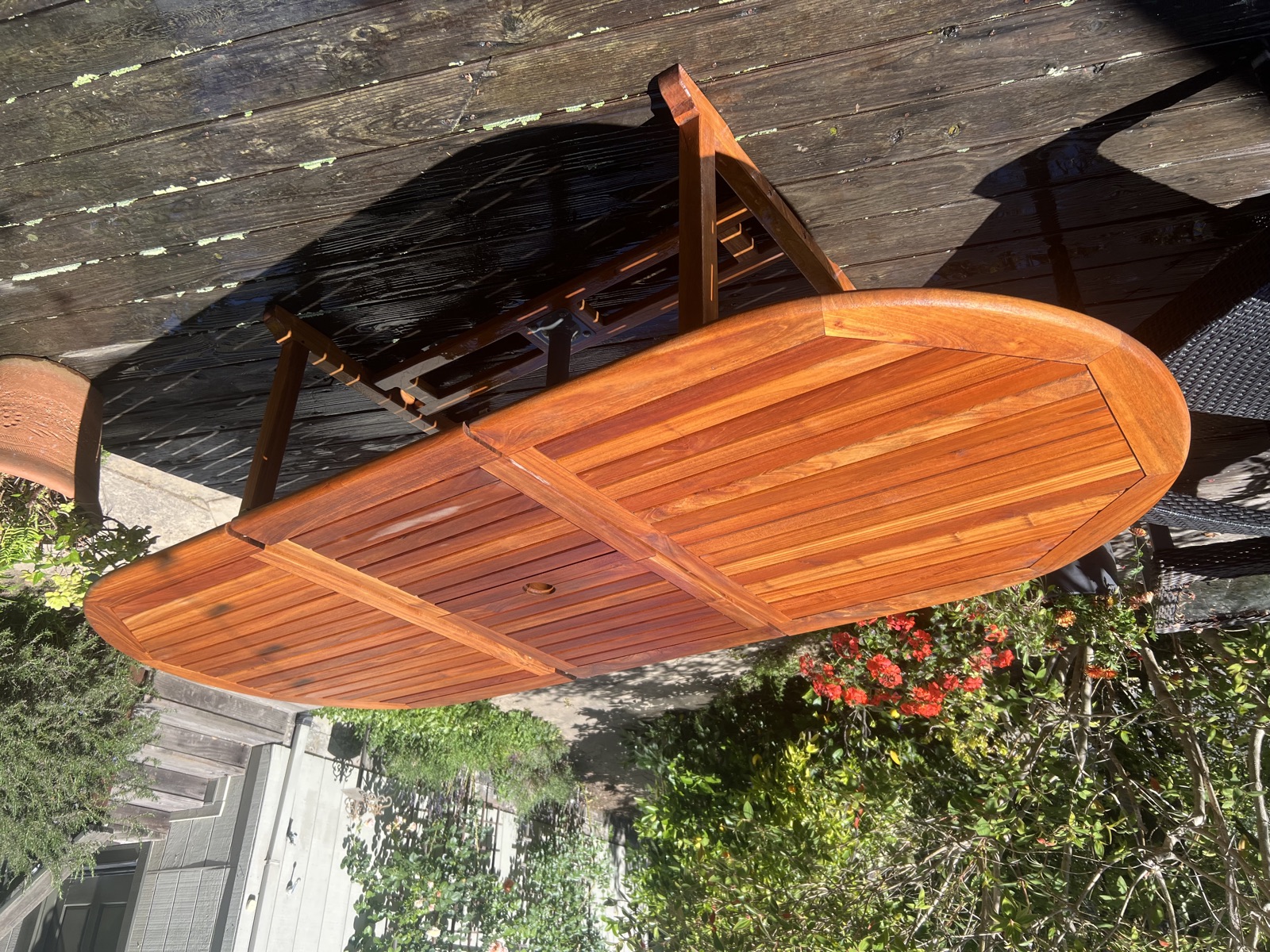 A restored teak patio table with a rich, deep finish in a garden setting